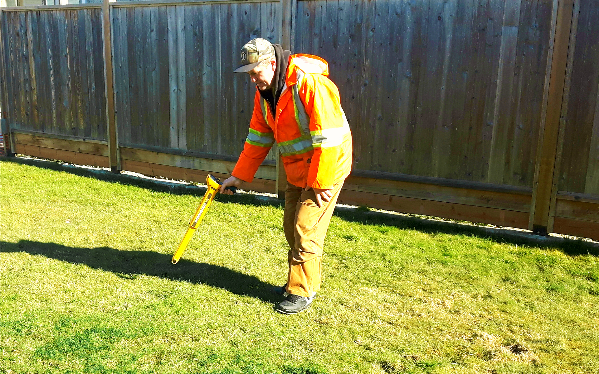 A worker uses a scanning device across a lawn to search for oil tanks buried below ground
